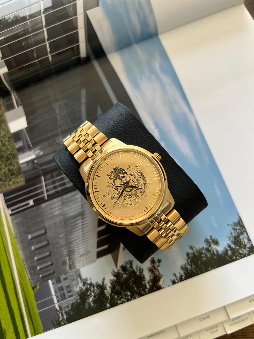 Reloj dorado con el escudo nacional y la carátula de la Heroica Escuela Naval Militar, fechada 2019 · 2024.
