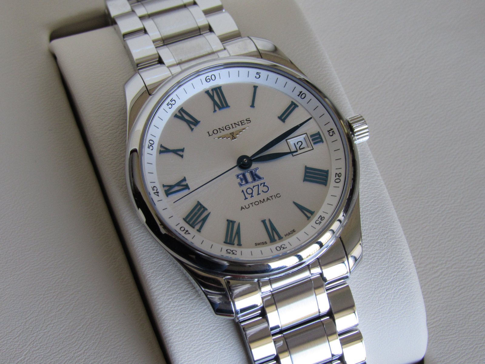 Reloj Longines Master Collection de acero, con esfera plateada, números romanos azules y el monograma EK sobre la fecha 1973.