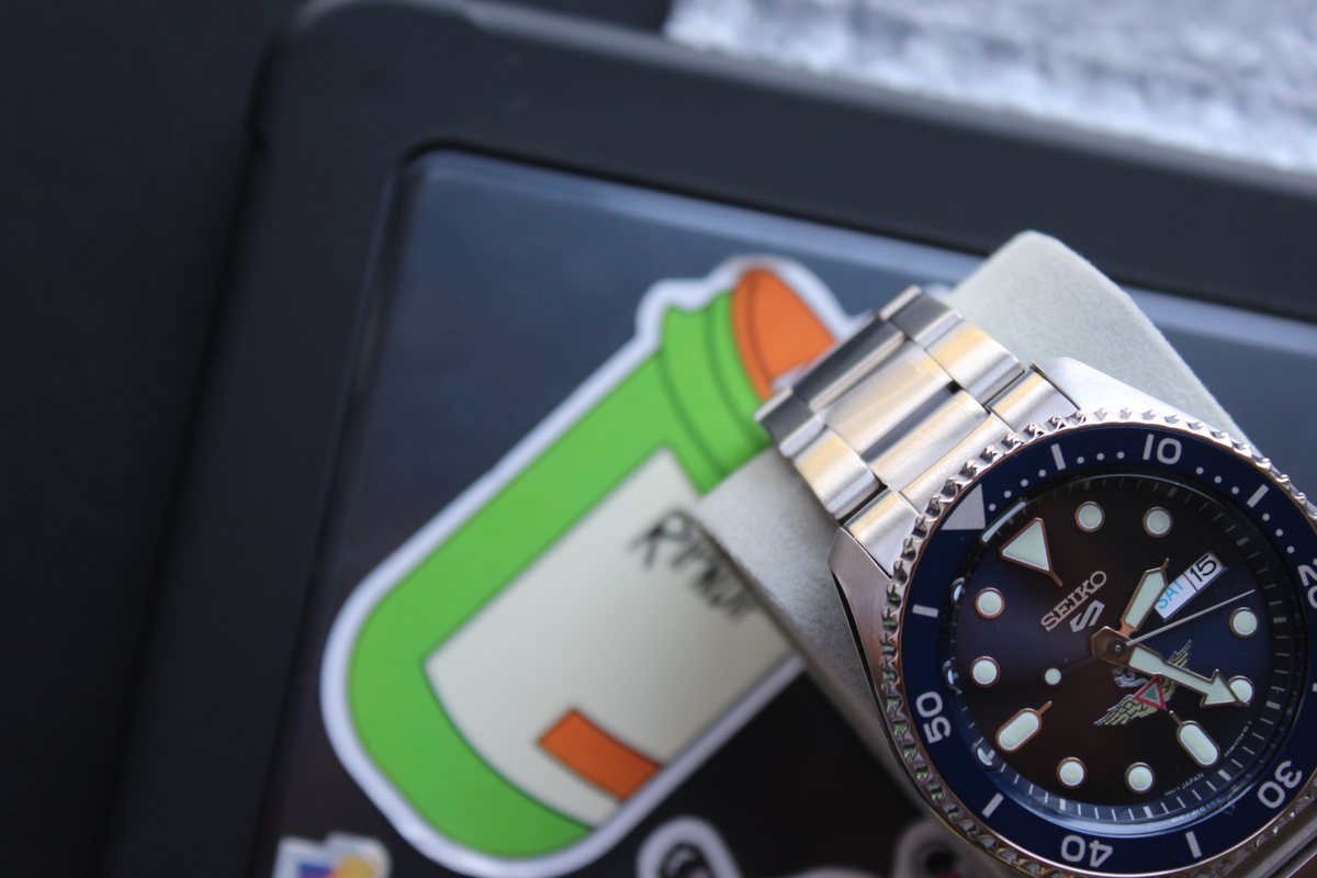 El reloj completo apoyado de perfil, con la esfera azul y el brazalete extendido.